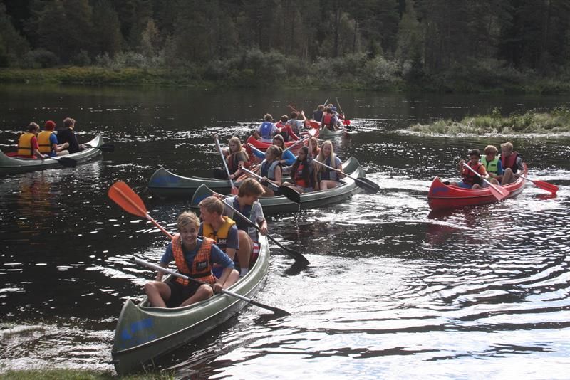Eight canoes with three young people in each, paddling in the river