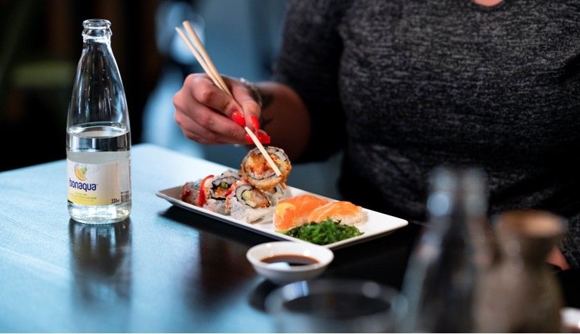 Talerken med sushi og en flaske med mineralvann ved siden av