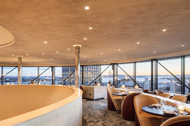 Tables and chairs in front of panoramic windows with a view of the city.