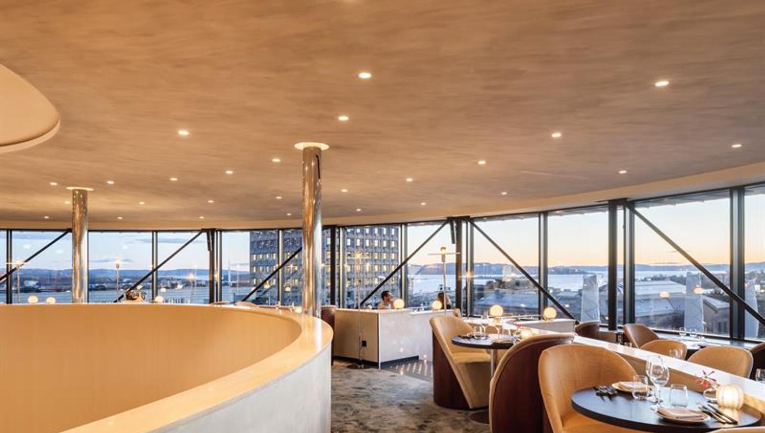 Tables and chairs in front of panoramic windows with a view of the city.