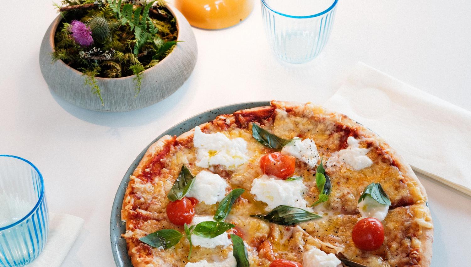 Stone oven-baked pizza with fresh basil, cherry tomatoes and soft cheese at Gløyp Spiseri.