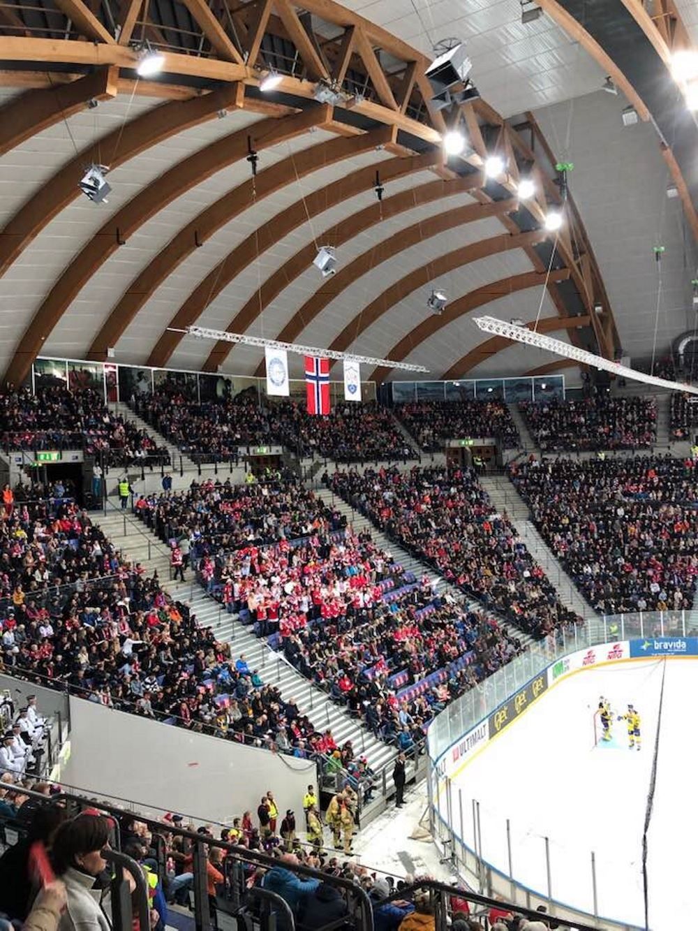 Innendørs ishockeyarena med buet tretak, fullsatte tribuner og en del av isbanen synlig nederst til høyre..