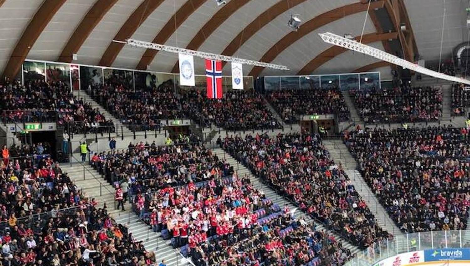 Innendørs ishockeyarena med buet tretak, fullsatte tribuner og en del av isbanen synlig nederst til høyre..