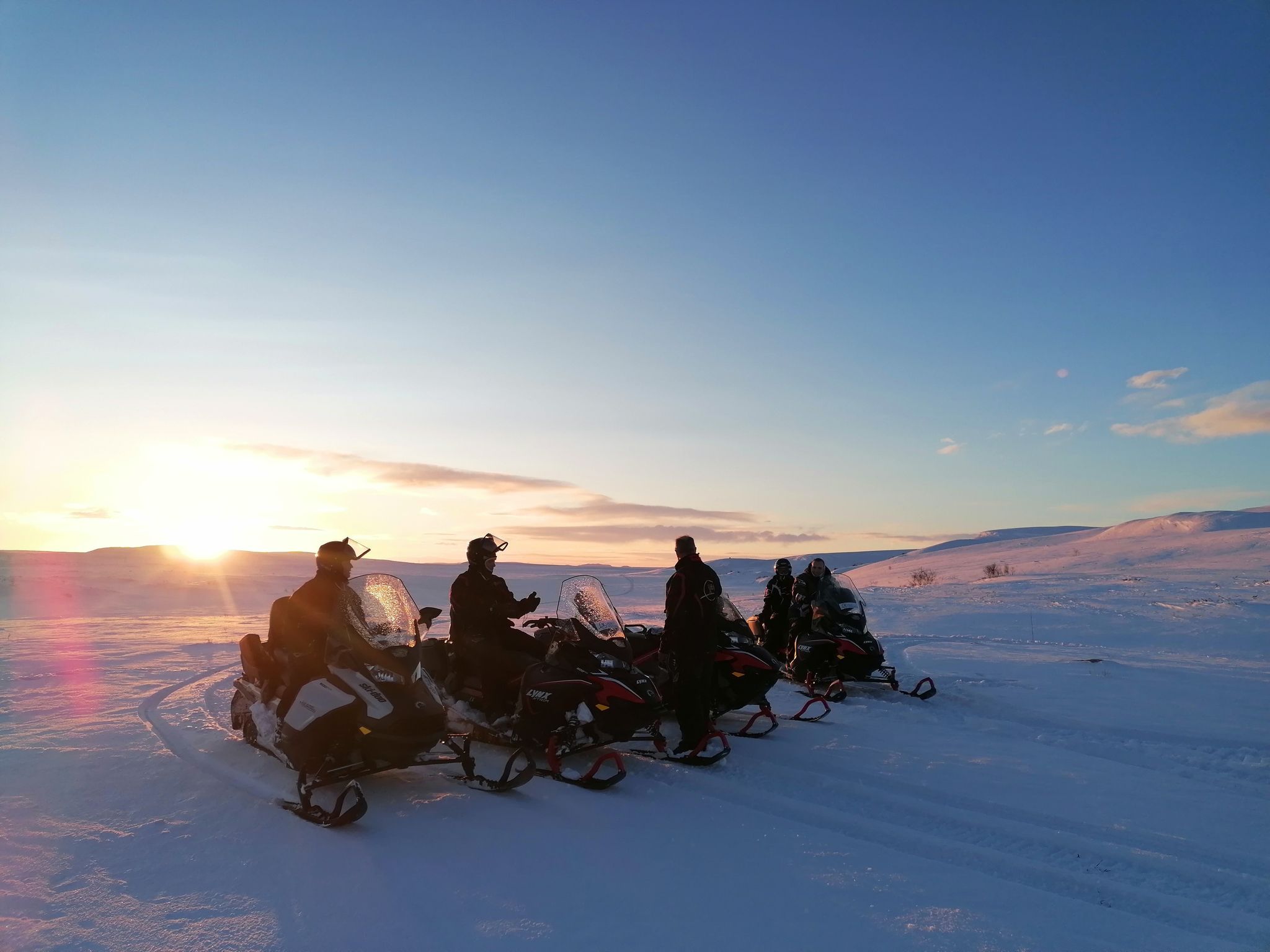Groupe de motoneigistes sur un paysage enneigé au lever du soleil.