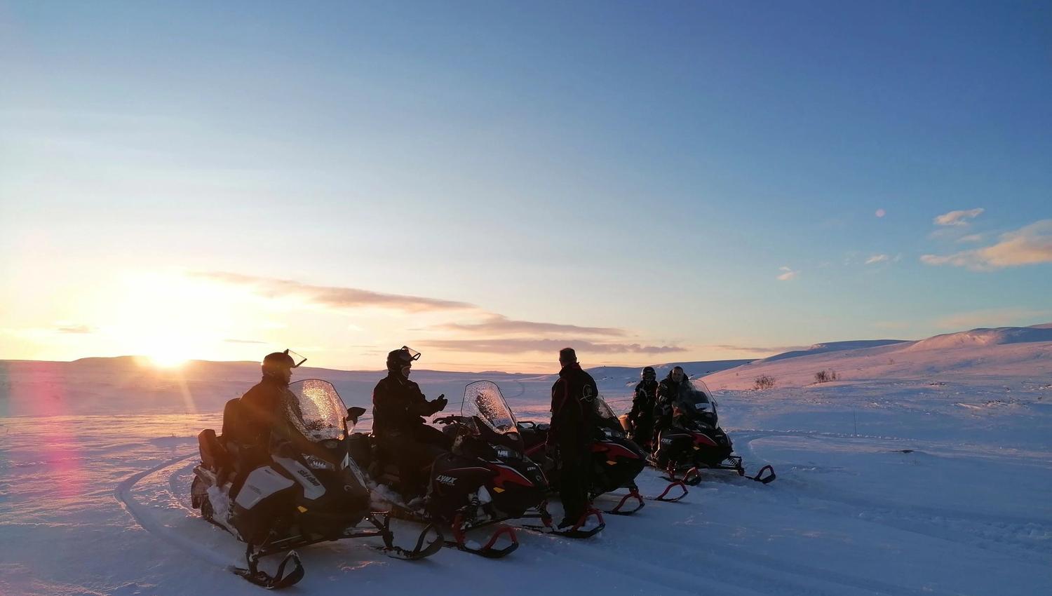 Groupe de motoneigistes sur un paysage enneigé au lever du soleil.