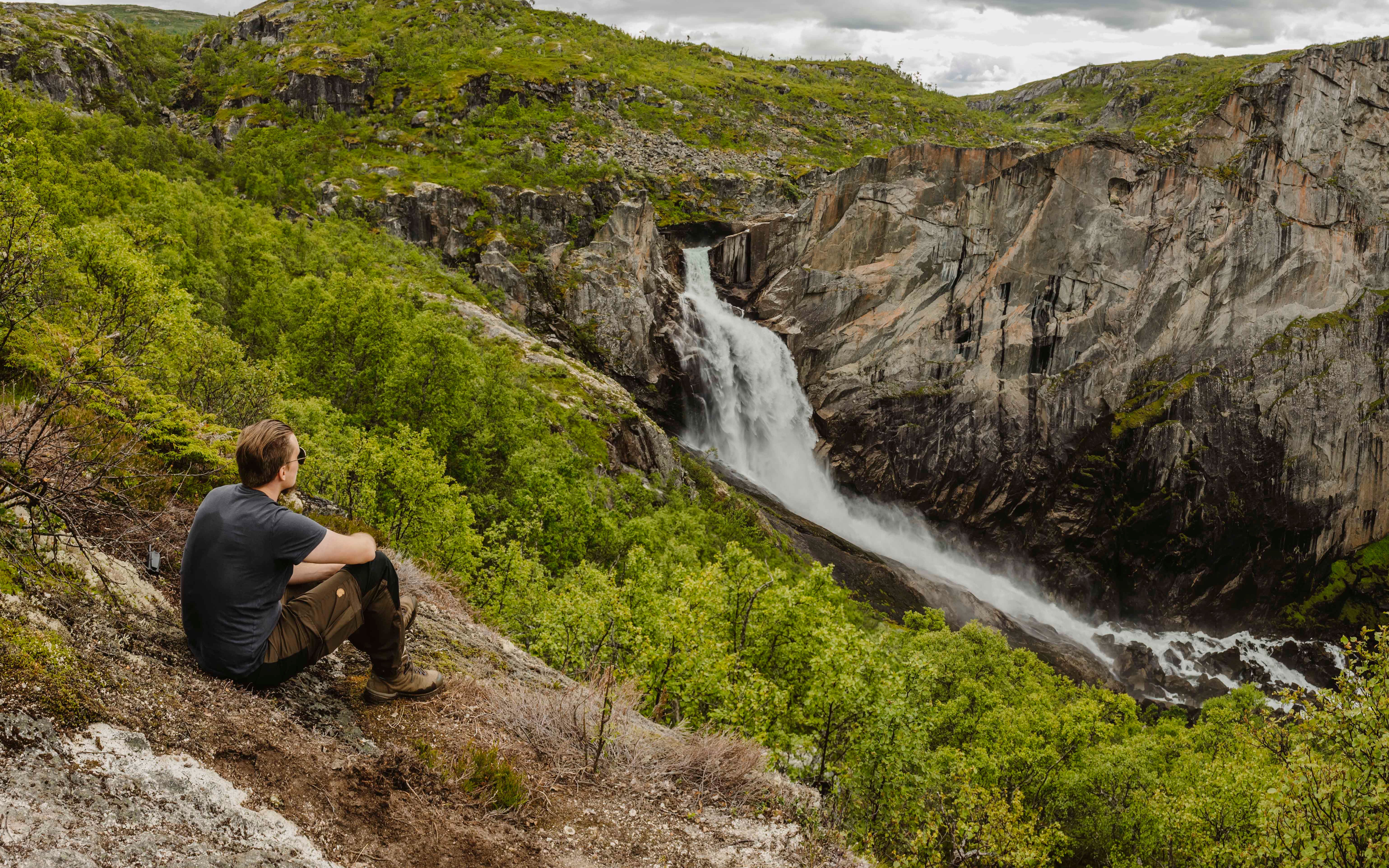 Ein Mann sitzt auf dem Boden und blickt auf den Wasserfall Valurfossen unten.