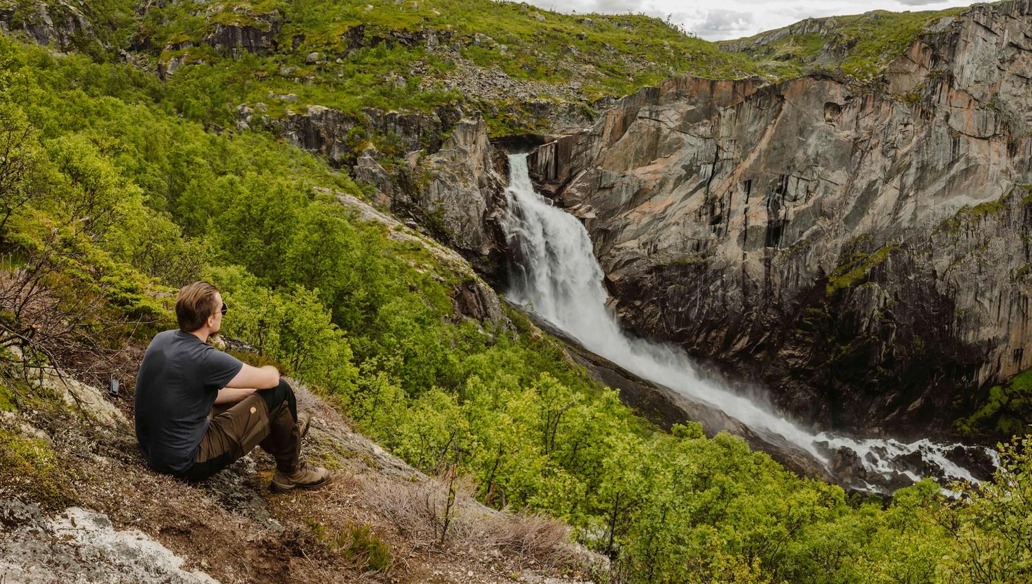 Ein Mann sitzt auf dem Boden und blickt auf den Wasserfall Valurfossen unten.
