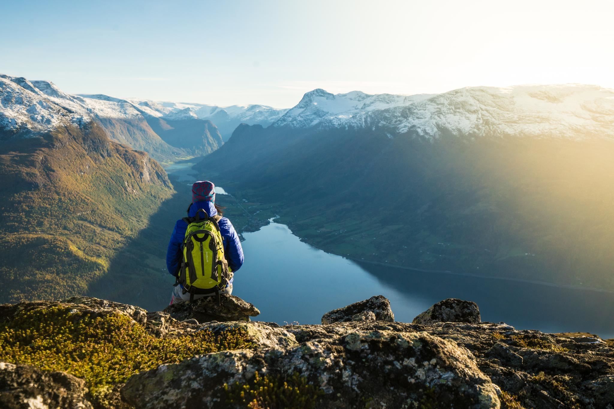 Hiker walking along a mountain trail at Hoven, with panoramic views of the fjord and surrounding mountains.