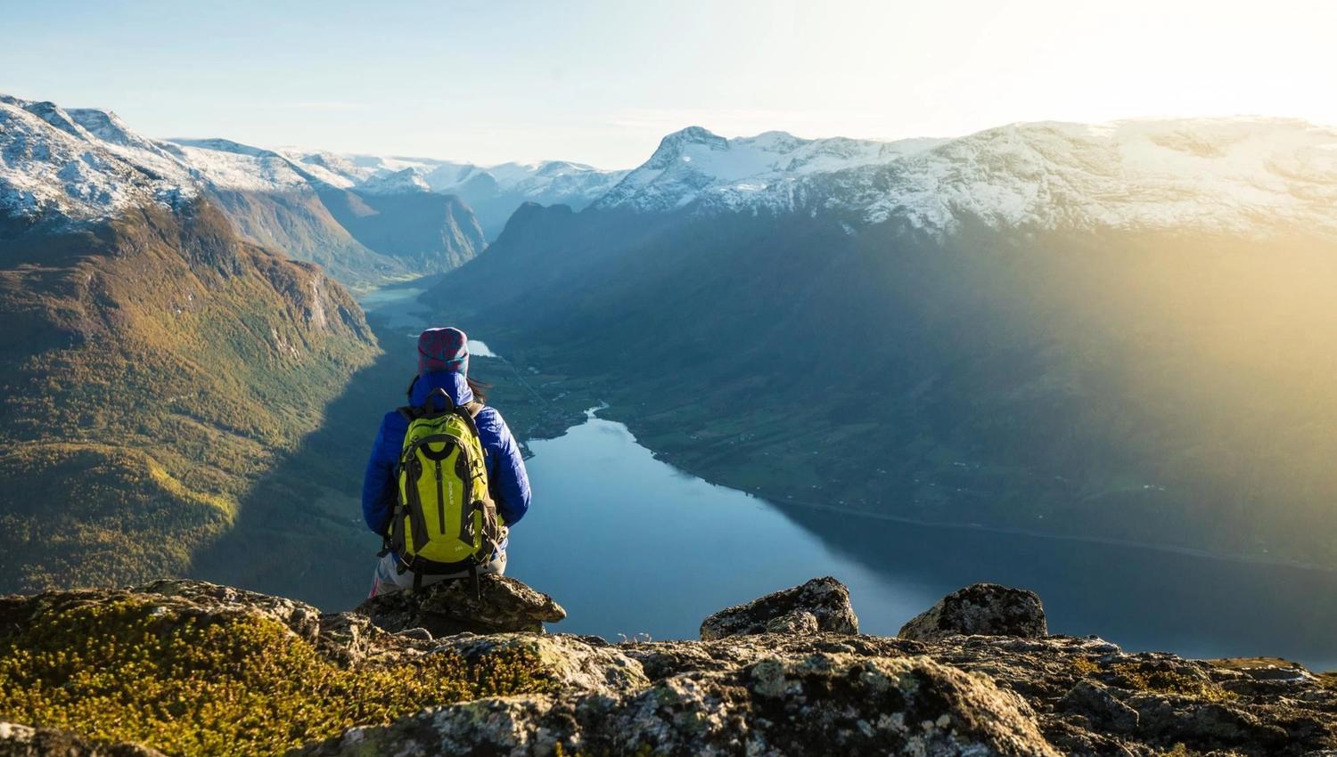 Hiker walking along a mountain trail at Hoven, with panoramic views of the fjord and surrounding mountains.