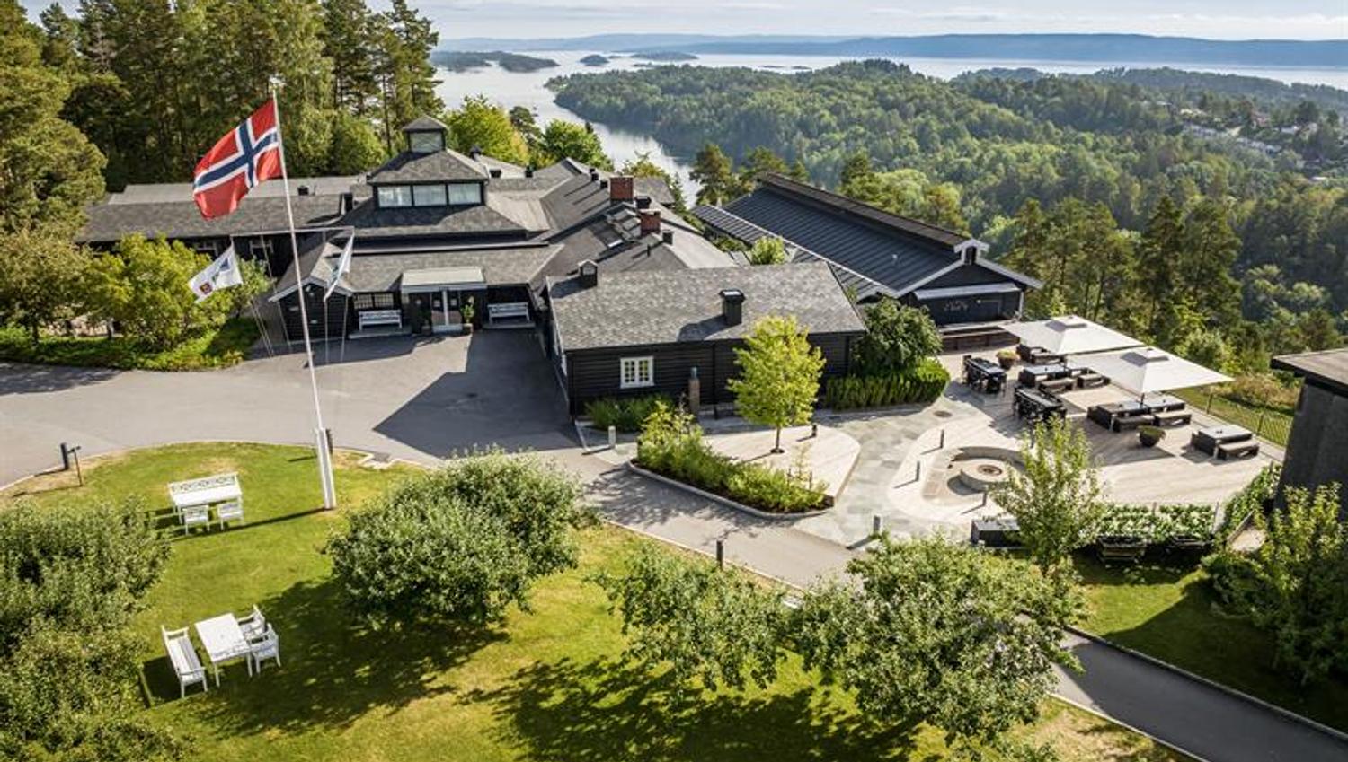 Oversiktsbilde av hotellet med fjord og skog i bakgrunn