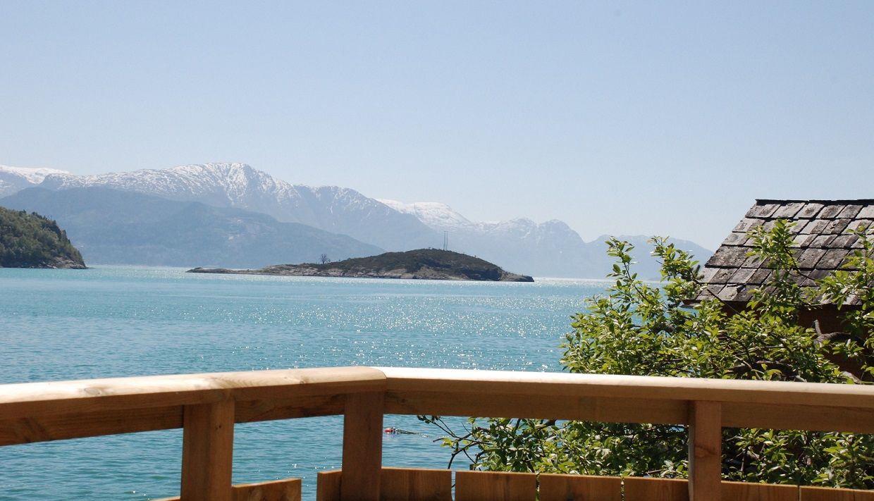 Sunny day by the Hardangerfjord viewed from the terrace – turquoise water and snow-capped peaks.