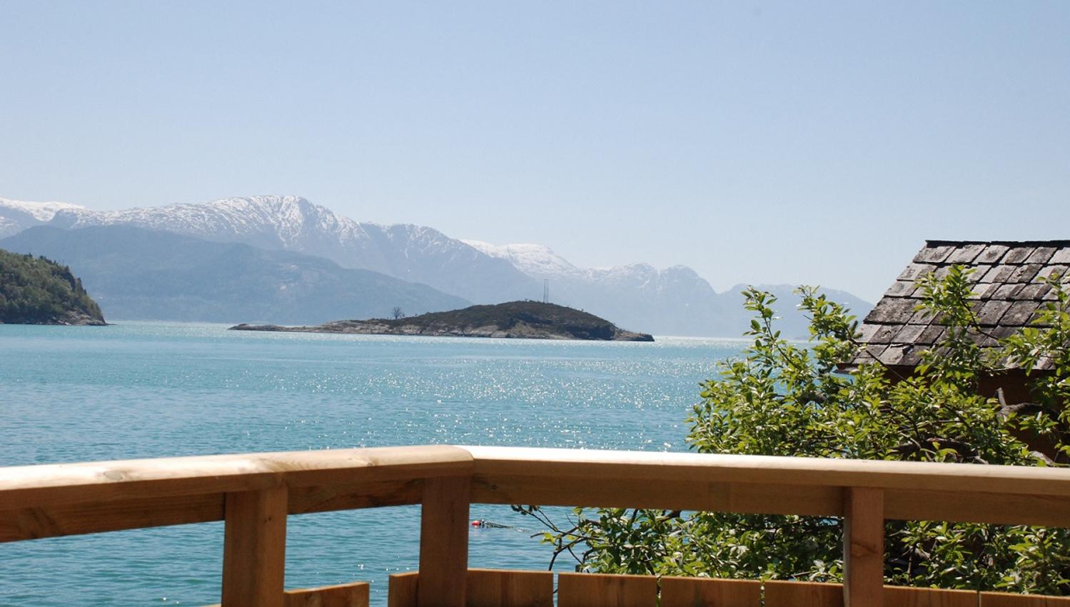 Sunny day by the Hardangerfjord viewed from the terrace – turquoise water and snow-capped peaks.