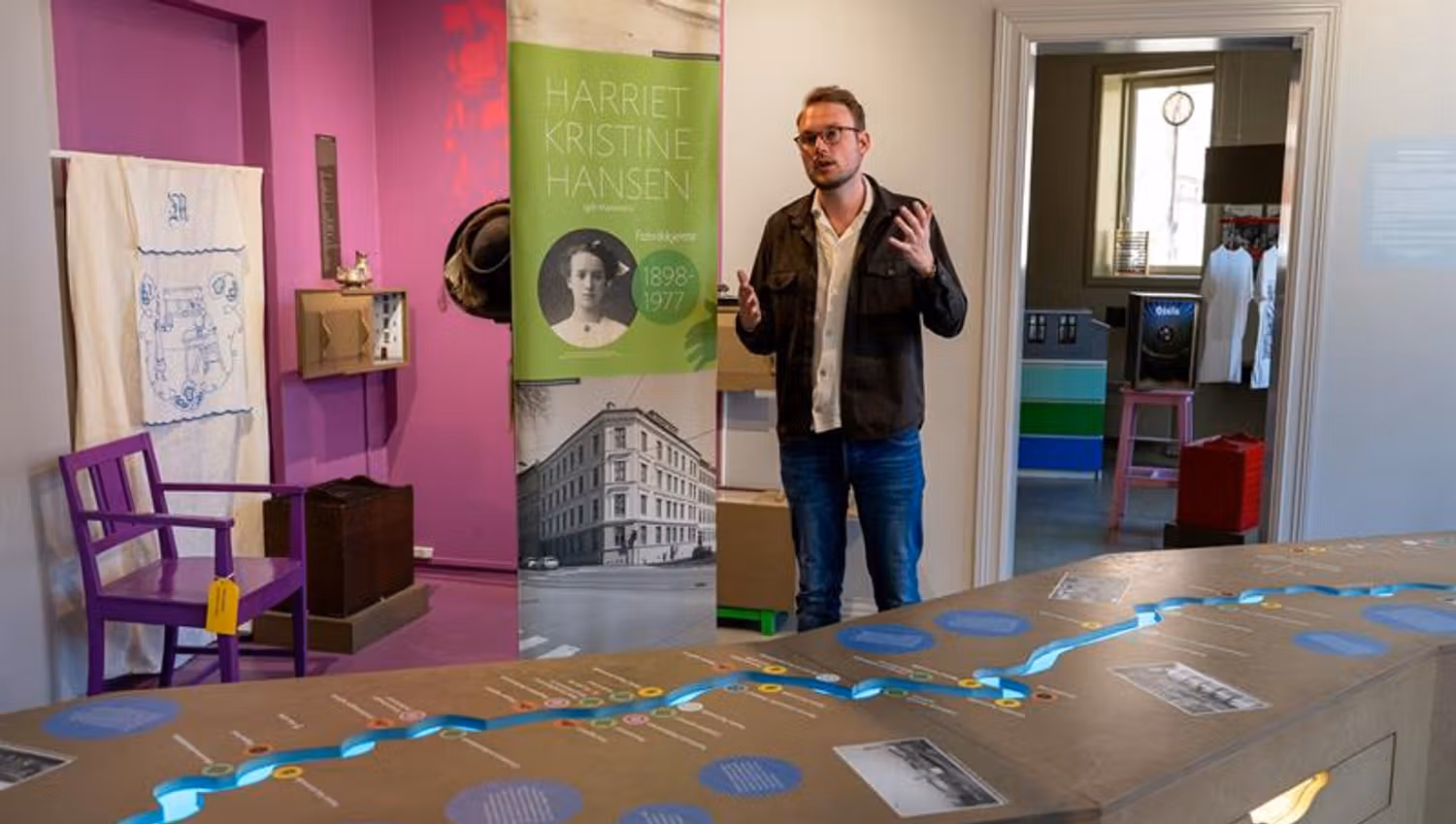 Person presenting a museum exhibition about Harriet Kristine Hansen, surrounded by historic photographs, objects and interactive elements.