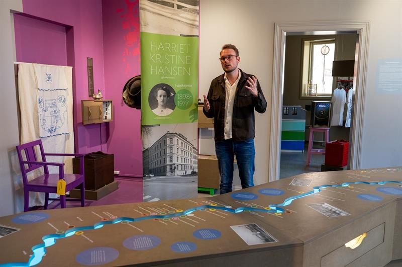 Person presenting a museum exhibition about Harriet Kristine Hansen, surrounded by historic photographs, objects and interactive elements.