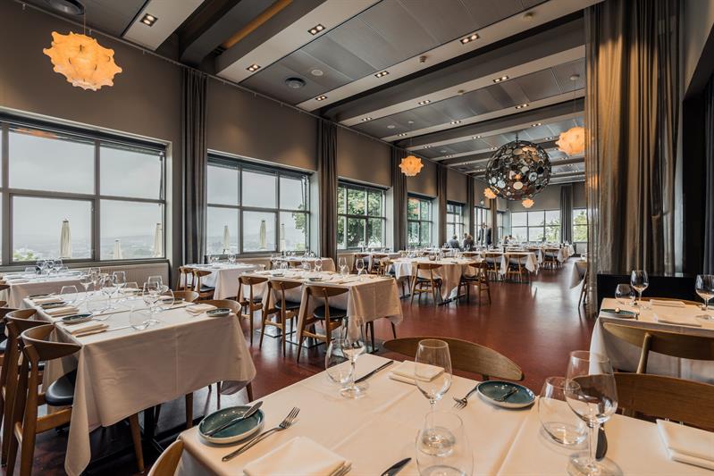 Elegant restaurantlokale med hvitdukede bord, store vinduer og moderne belysning.