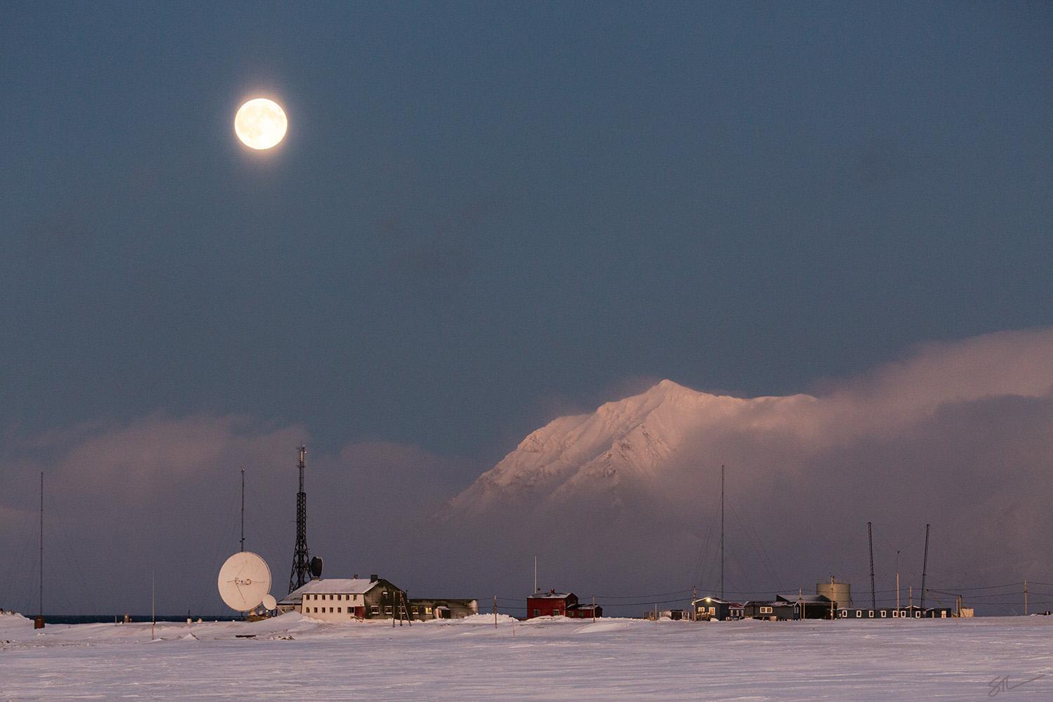 Isfjord Radio i vinterlandskap med tåke over fjorden i bakgrunnen og månen som skinner på himmelen.