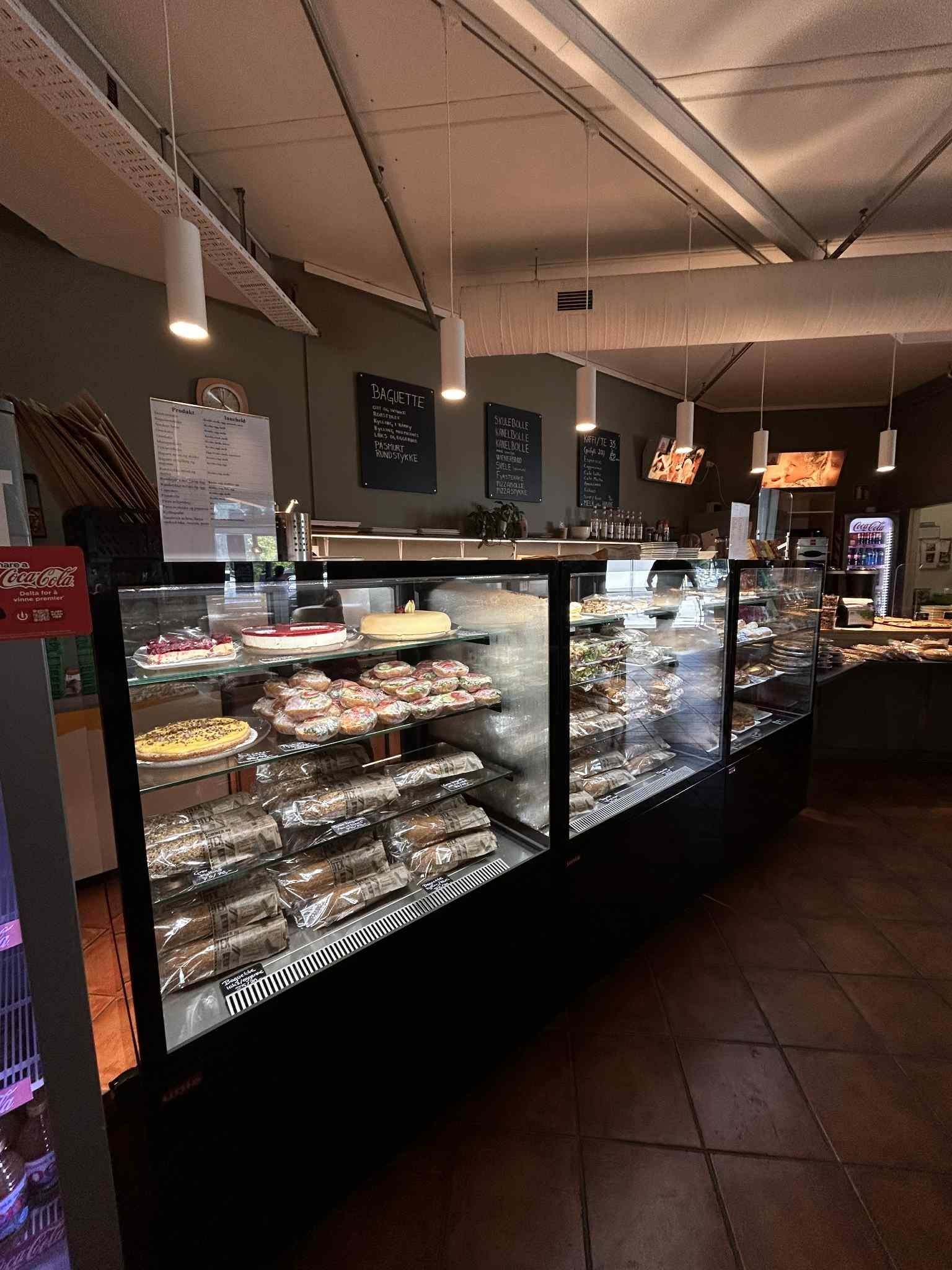 Interior of a bakery or cafe with glass display cases filled with pastries and cakes, and menu boards on the wall.