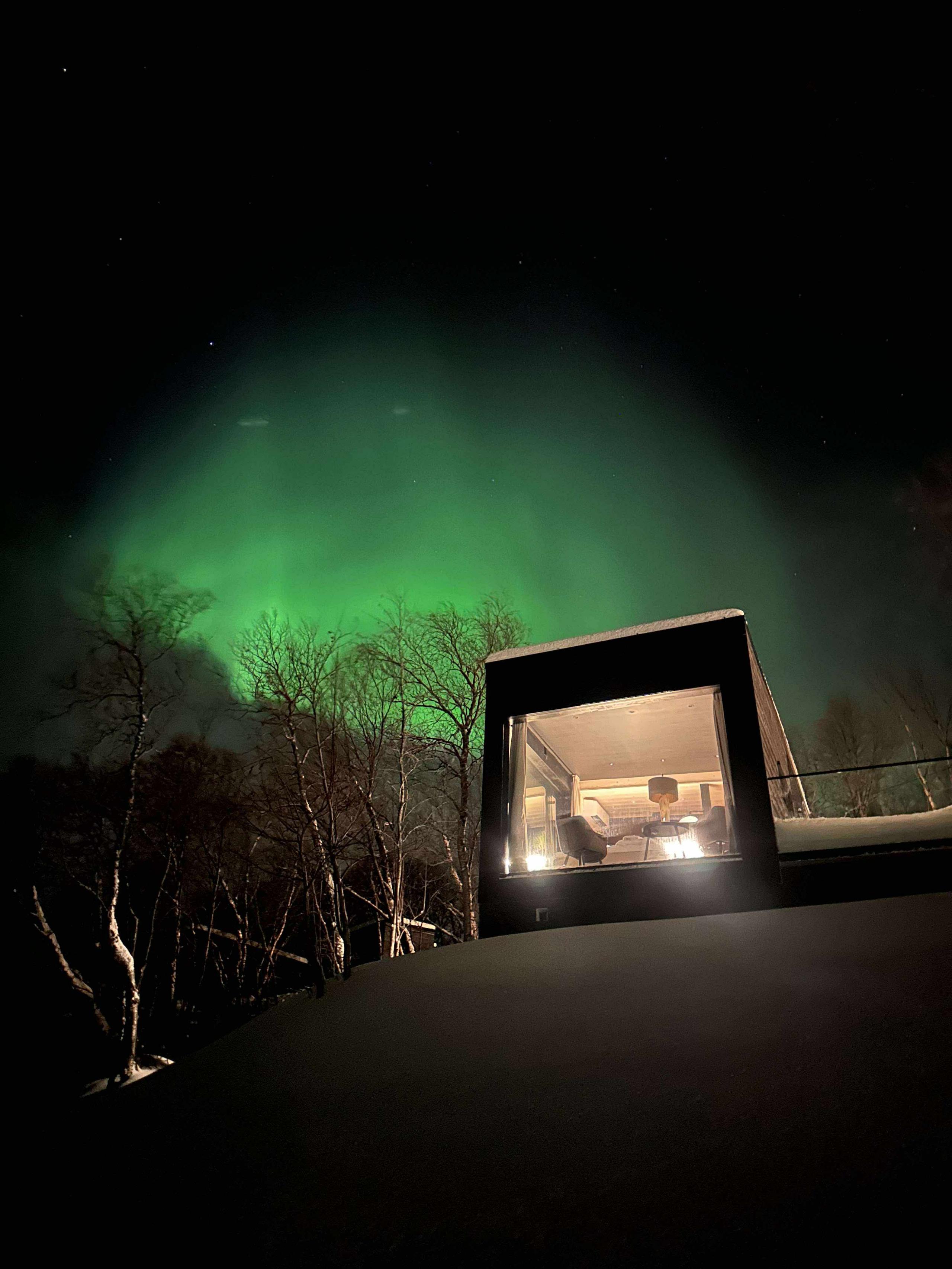 Lichtgevende aurora borealis boven een moderne hut in de sneeuw.