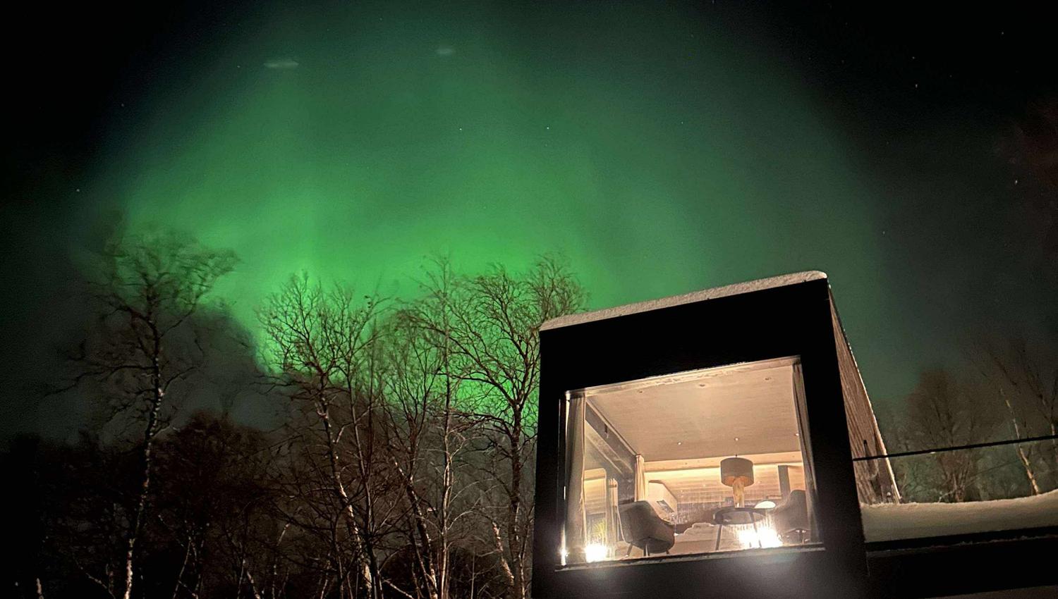 Lichtgevende aurora borealis boven een moderne hut in de sneeuw.