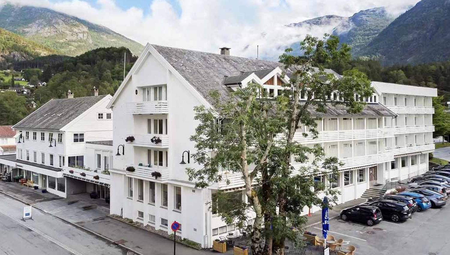 The facade of Kinsarvik Fjordhotel with scenic views of the Hardangerfjord, surrounded by beautiful nature and mountain landscape.