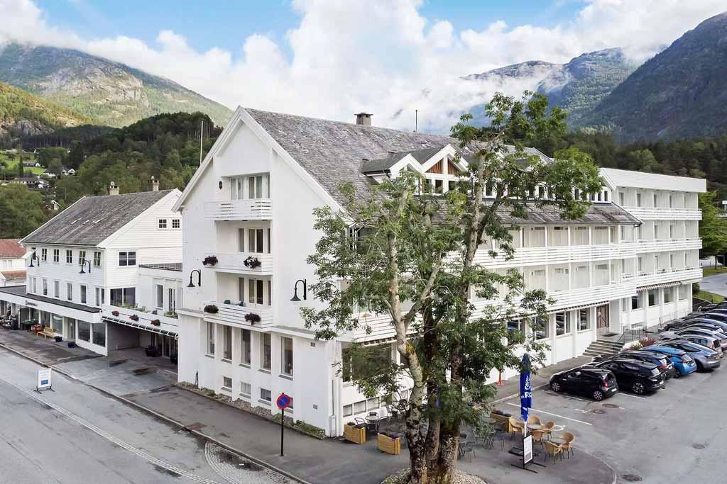The facade of Kinsarvik Fjordhotel with scenic views of the Hardangerfjord, surrounded by beautiful nature and mountain landscape.