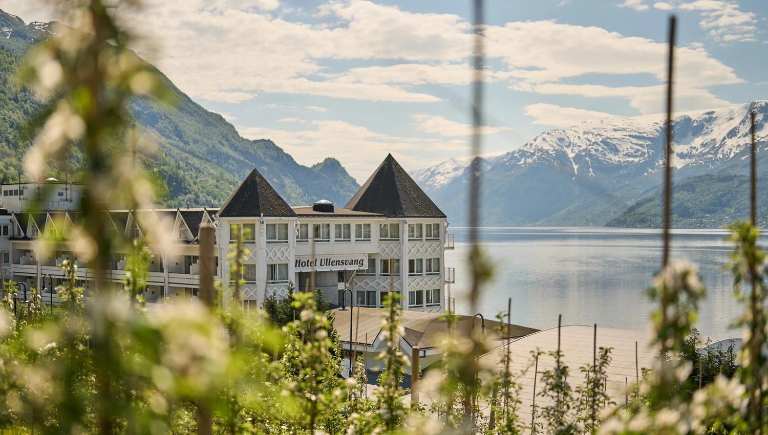Hotel Ullensvang seen through blooming fruit trees – a springtime idyll by the fjord.