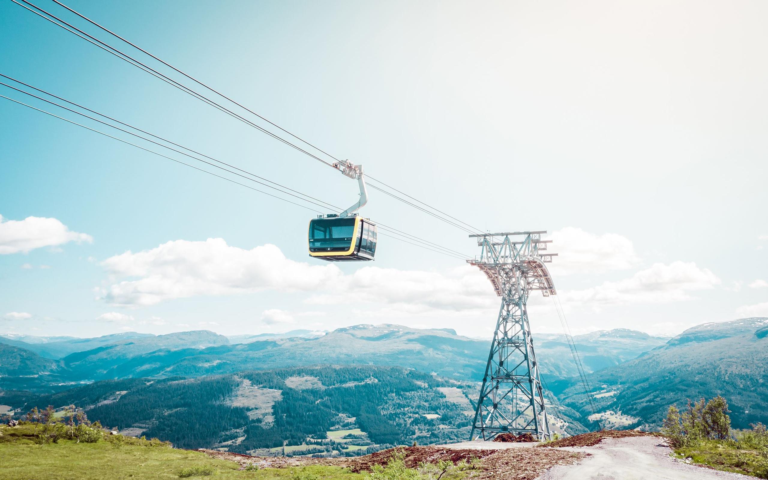 A gondola gliding along the cable line high above the landscape, with rolling mountains stretching into the distance.