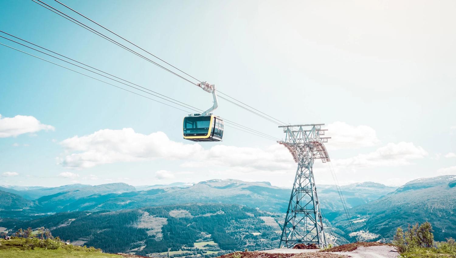 A gondola gliding along the cable line high above the landscape, with rolling mountains stretching into the distance.
