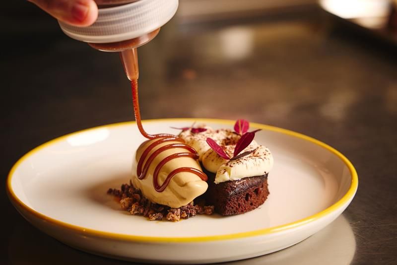 Detail of chocolate sauce being poured over a dessert in a bowl