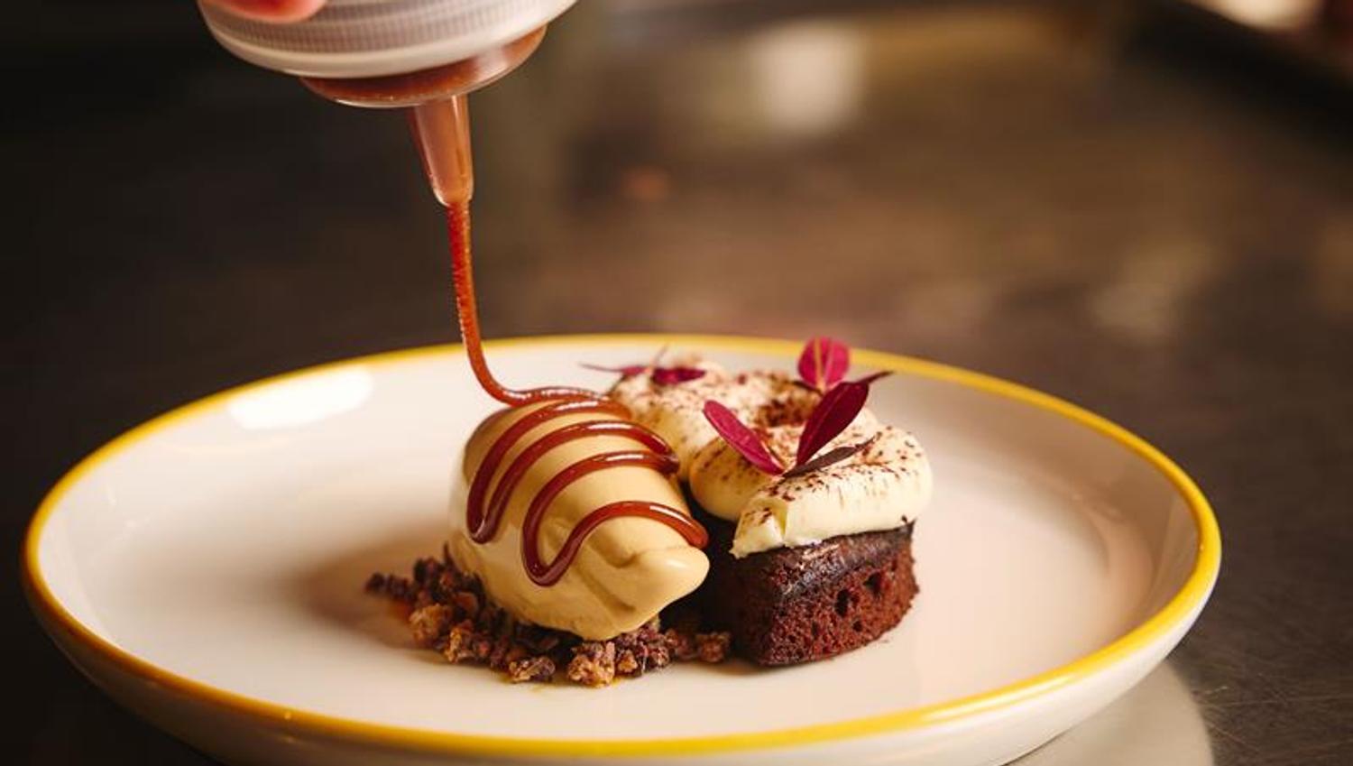 Detail of chocolate sauce being poured over a dessert in a bowl