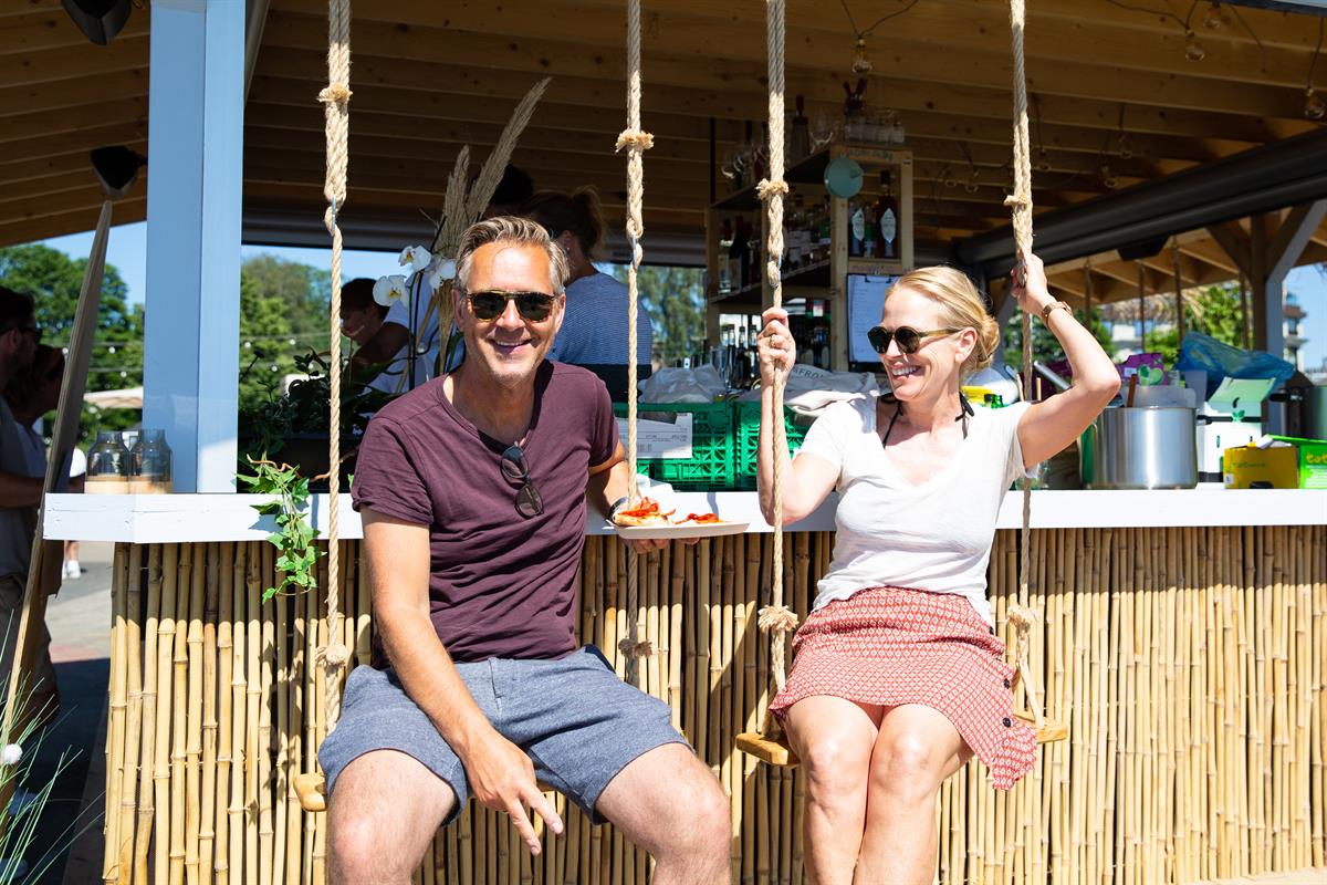 To personer sitter i husker ved en strandbar under et stråtak.