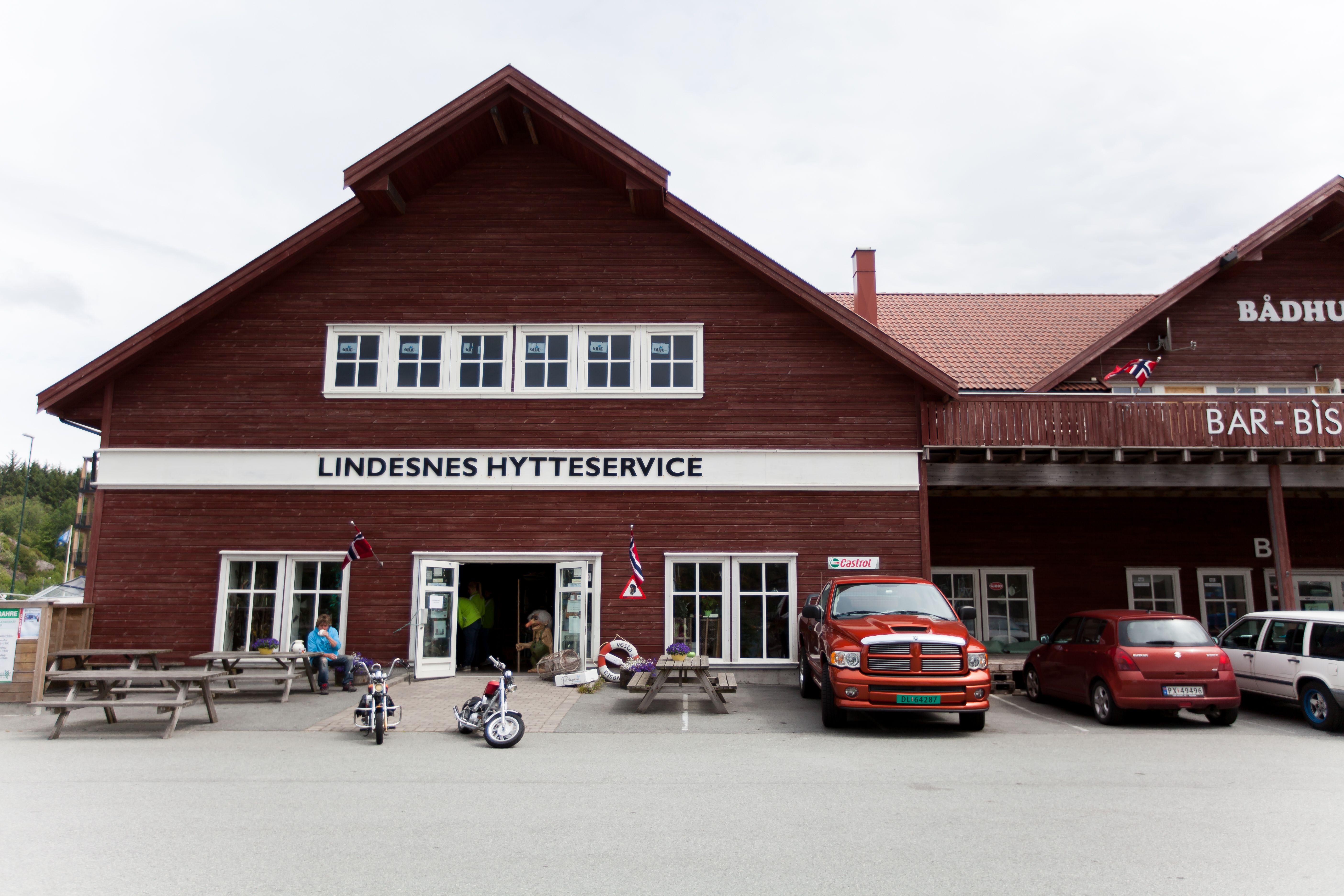 Lindesnes Hytteservice – Facade. Reddish-brown building with benches outside.