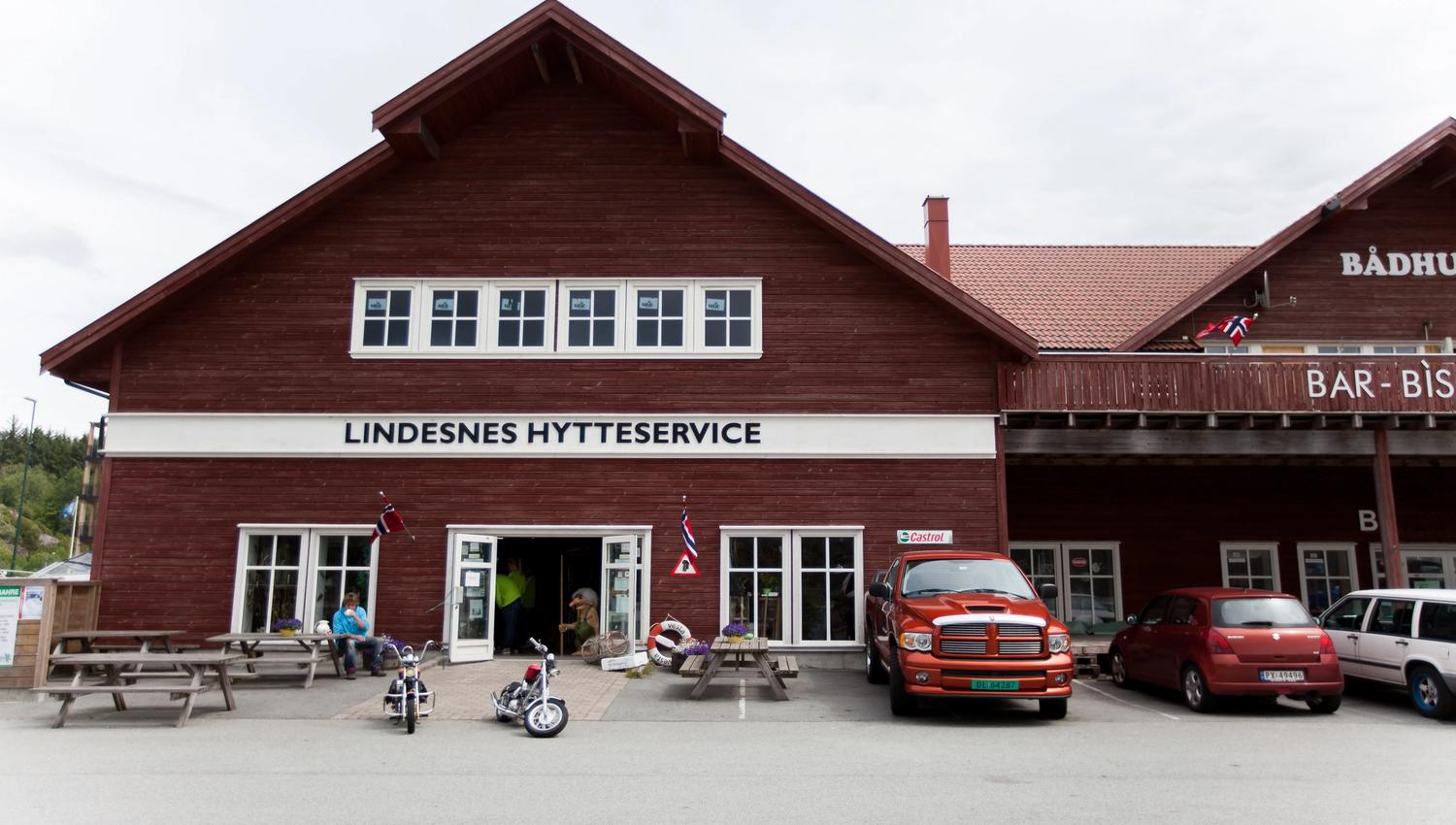 Lindesnes Hytteservice – Facade. Reddish-brown building with benches outside.