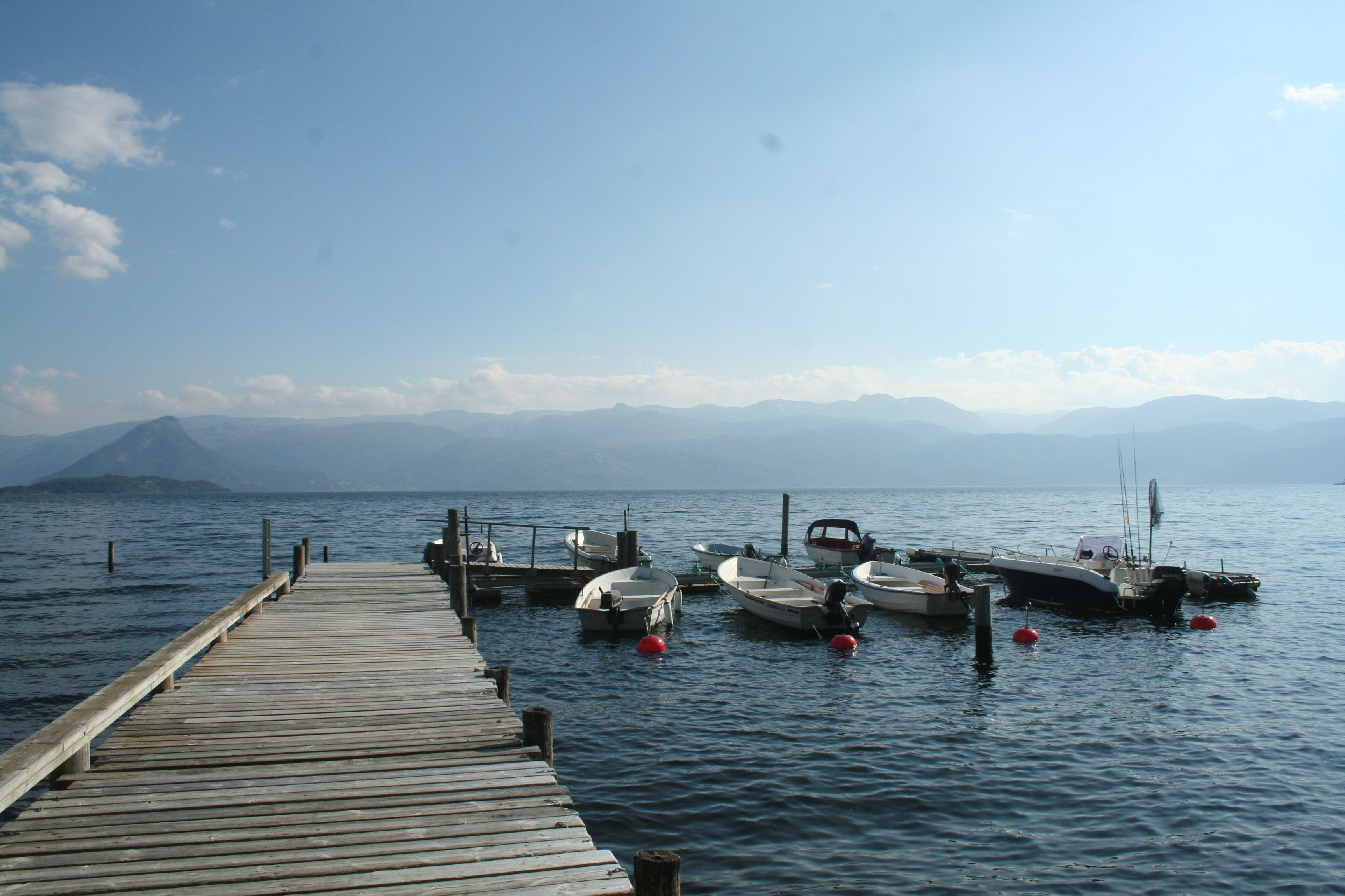 Wooden pier with small boats at Hardanger Feriesenter, surrounded by mountains and fjord.