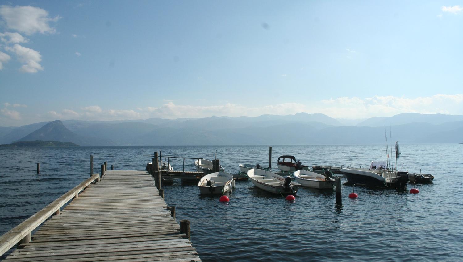Wooden pier with small boats at Hardanger Feriesenter, surrounded by mountains and fjord.