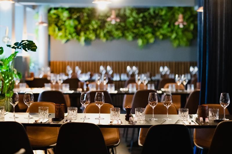 Long tables set for dining, orange chairs and vegetation along the wall