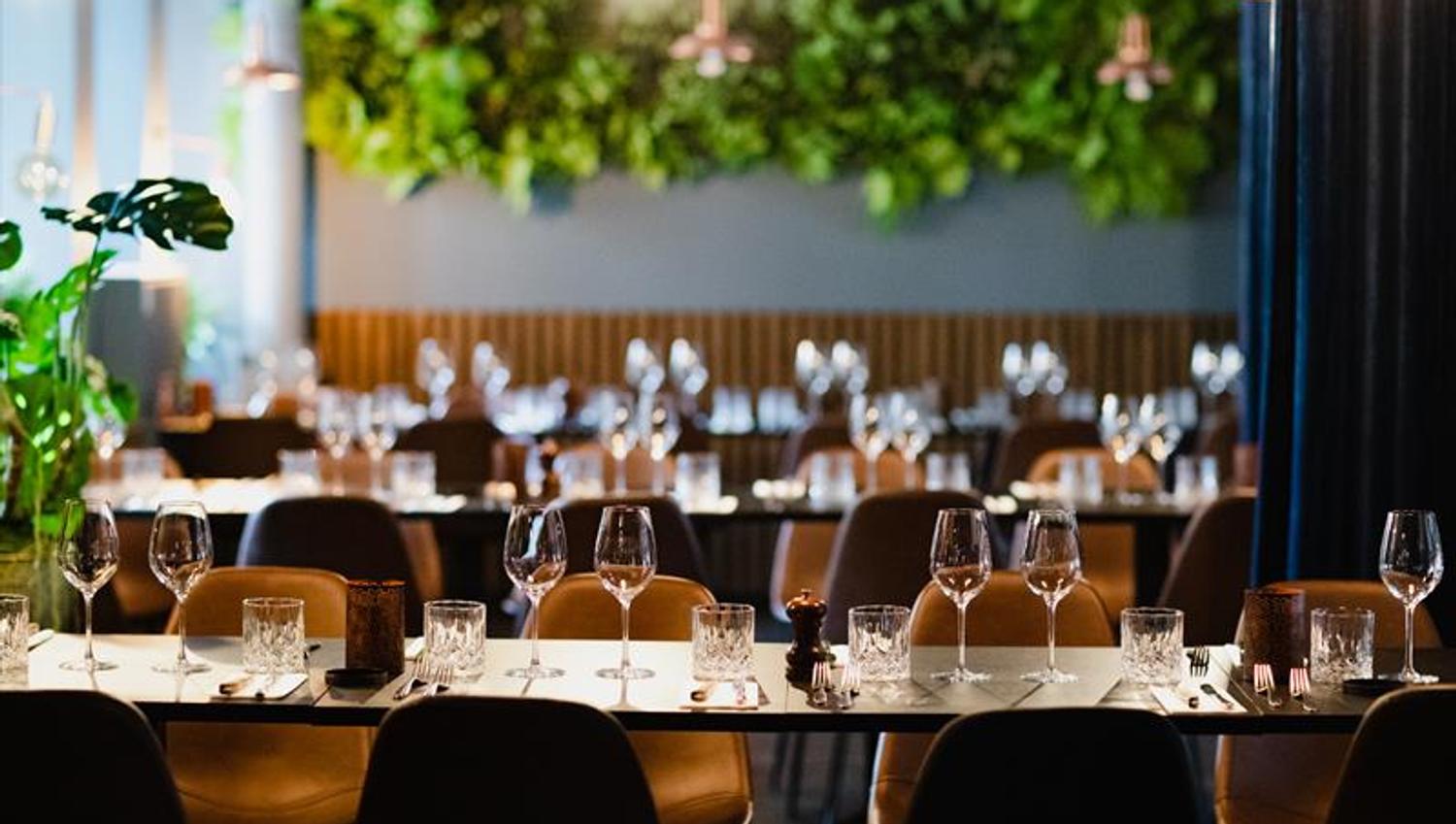 Long tables set for dining, orange chairs and vegetation along the wall