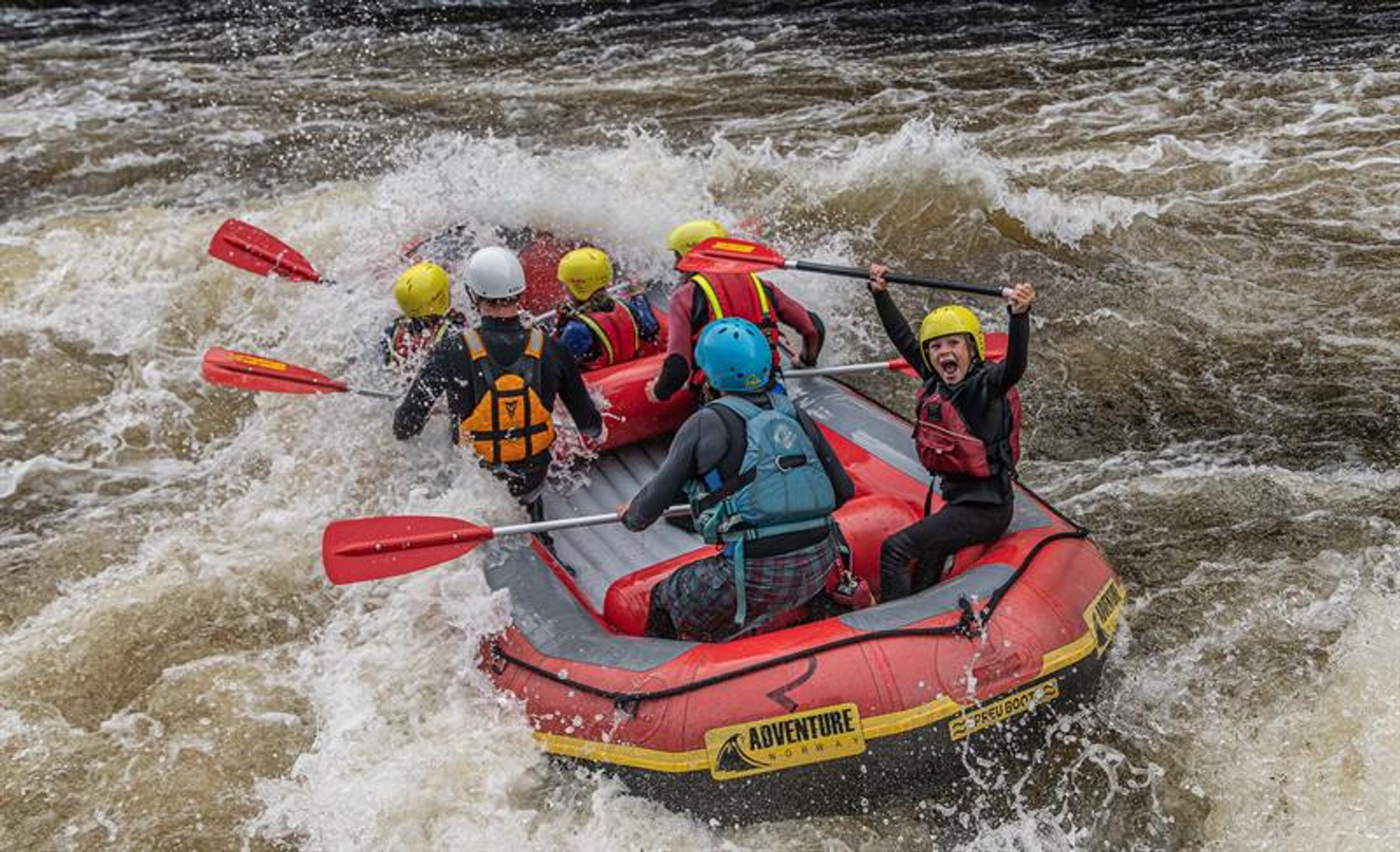 Rafting on the Mandalselva River, a happy group riding the waves. A child shouting with joy, lifting the paddle above their head.