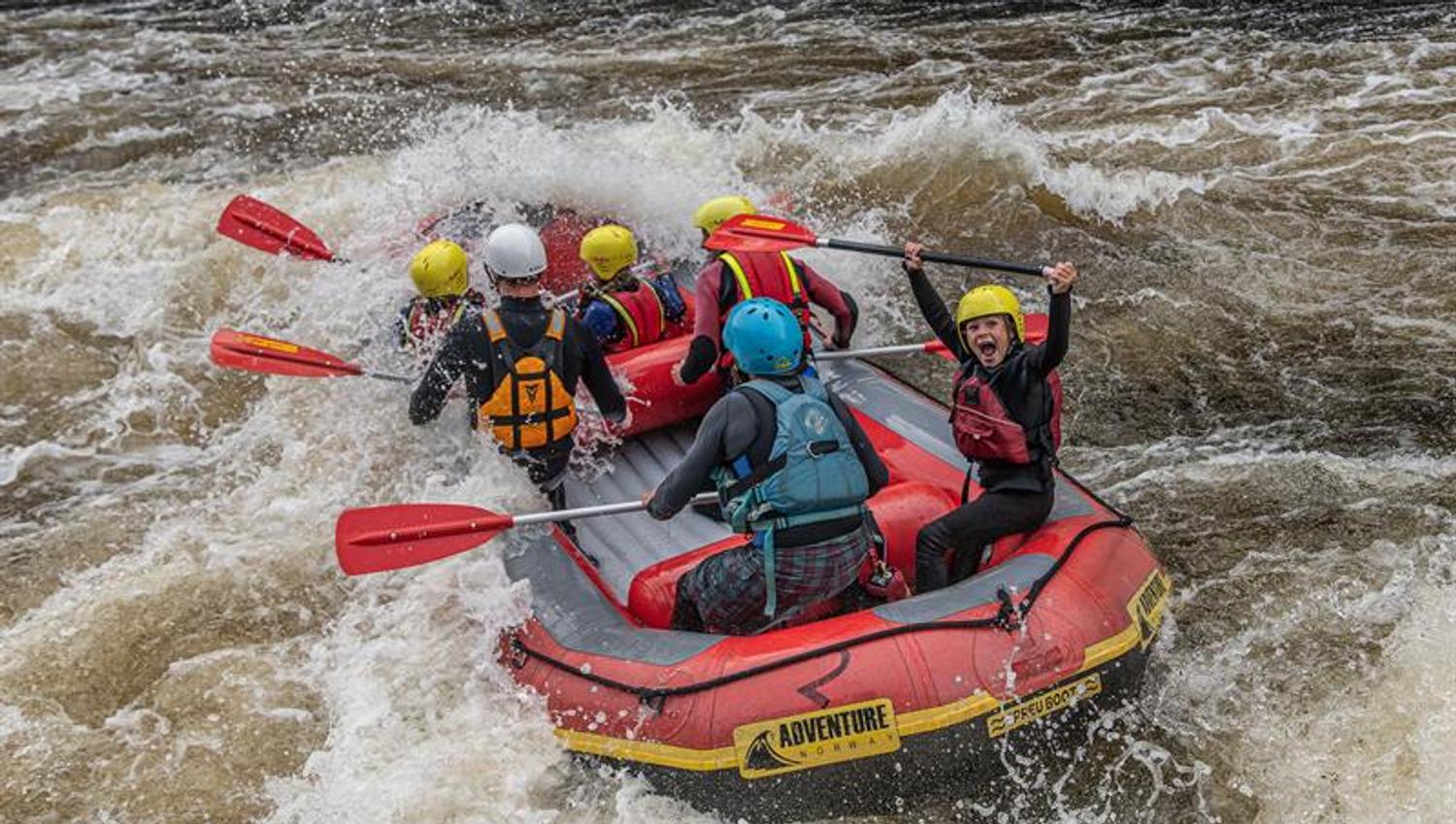 Rafting on the Mandalselva River, a happy group riding the waves. A child shouting with joy, lifting the paddle above their head.