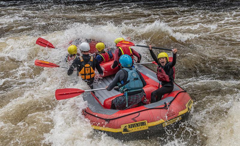 Rafting on the Mandalselva River, a happy group riding the waves. A child shouting with joy, lifting the paddle above their head.