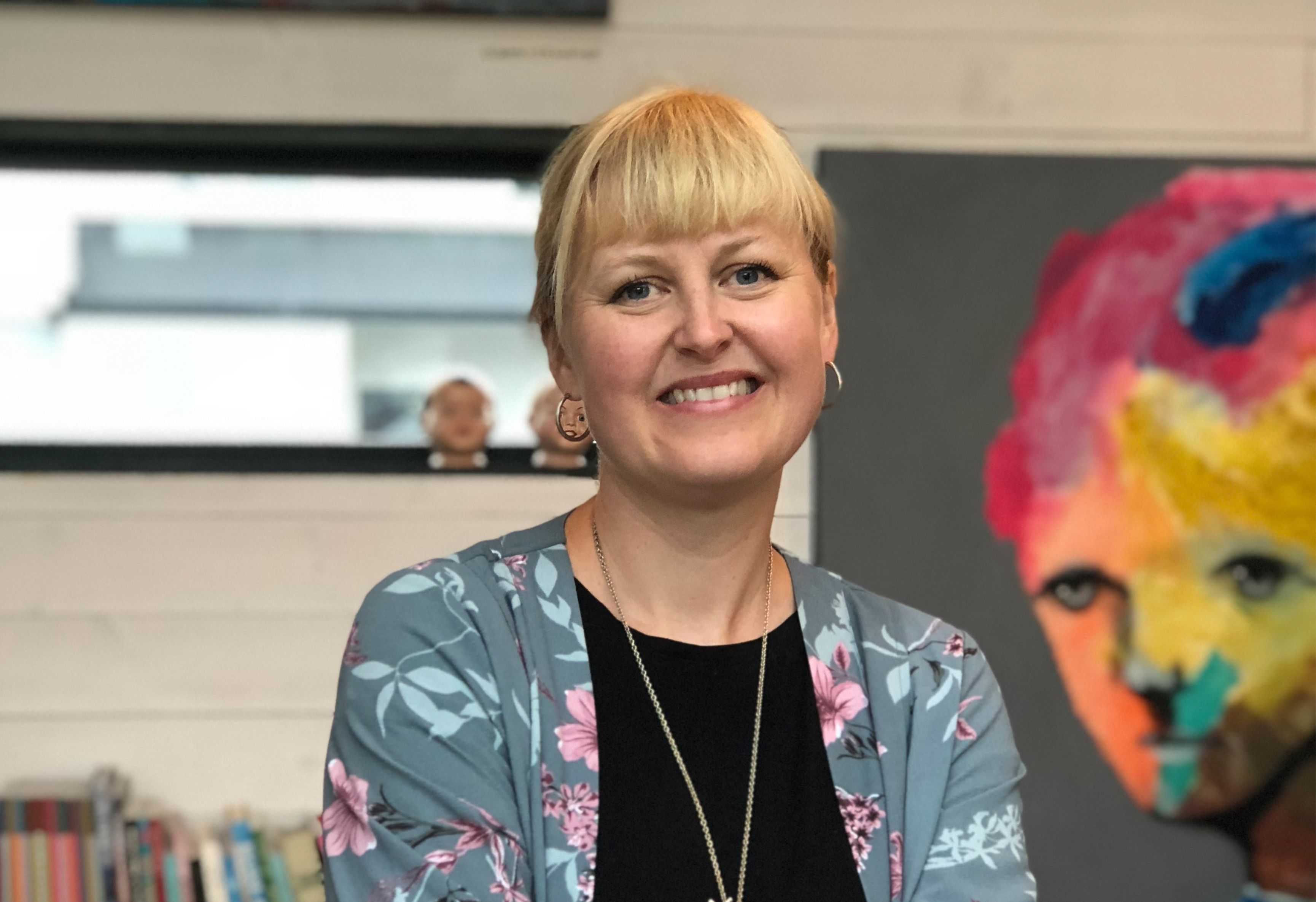 Portrait of a woman with light hair, with art on the wall behind her