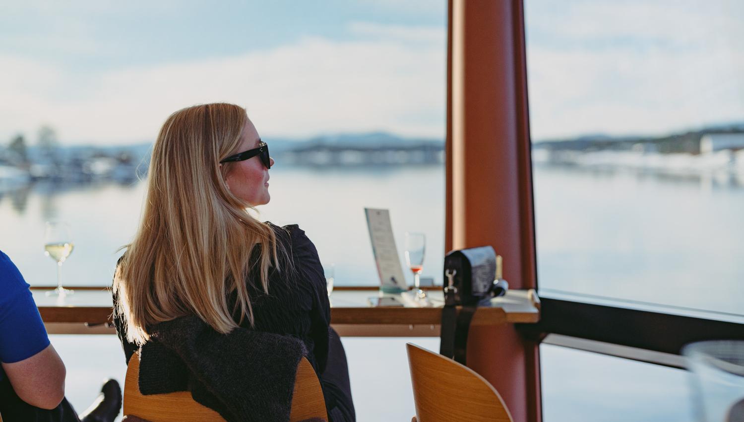 Jente som sitter inne i båten og ser på utsikten gjennom panoramavinduet