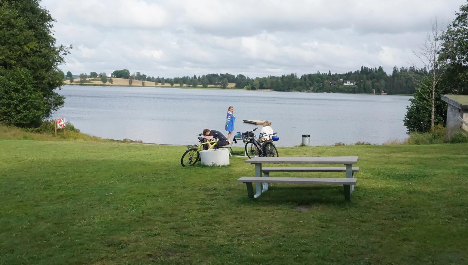 benk på plen ved vannet og folk på sykkel