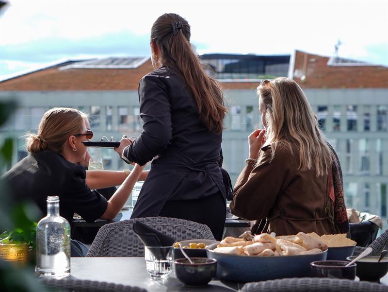 Guests enjoying food and drinks on a sunny rooftop terrace in Oslo.