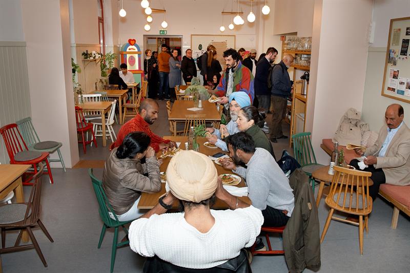 Café area with visitors seated at tables and people queueing near the serving area.