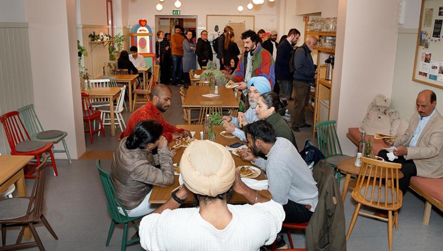 Café area with visitors seated at tables and people queueing near the serving area.