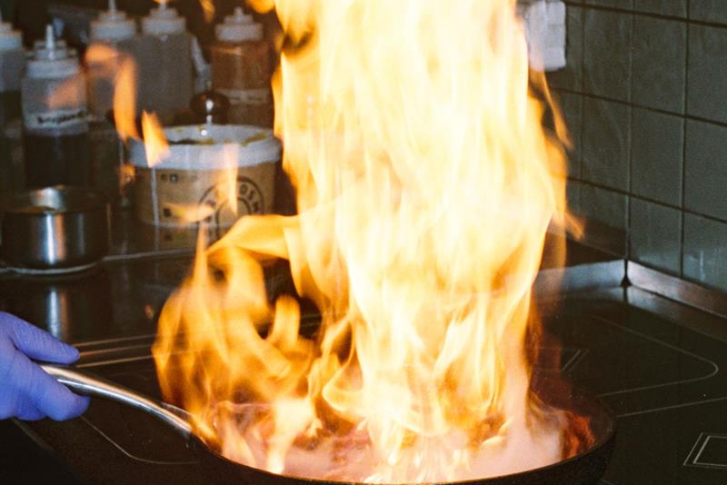 Flames rise from a pan on the hob during cooking in a professional restaurant kitchen.