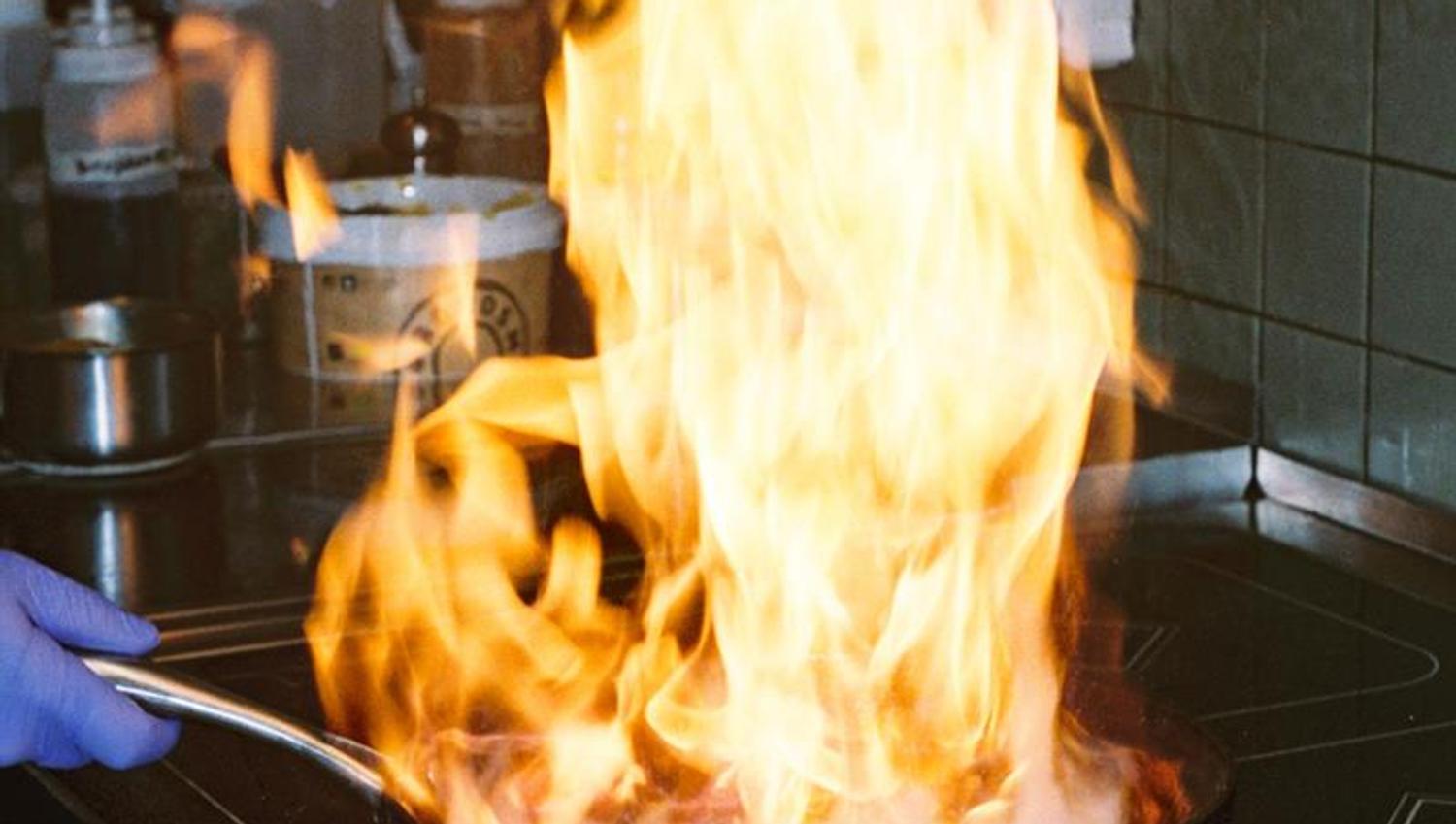 Flames rise from a pan on the hob during cooking in a professional restaurant kitchen.
