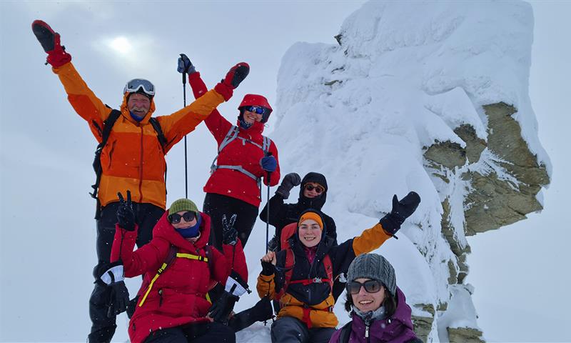 A group of guests cheering for the camera on top of Trollsteinen in snowy conditions