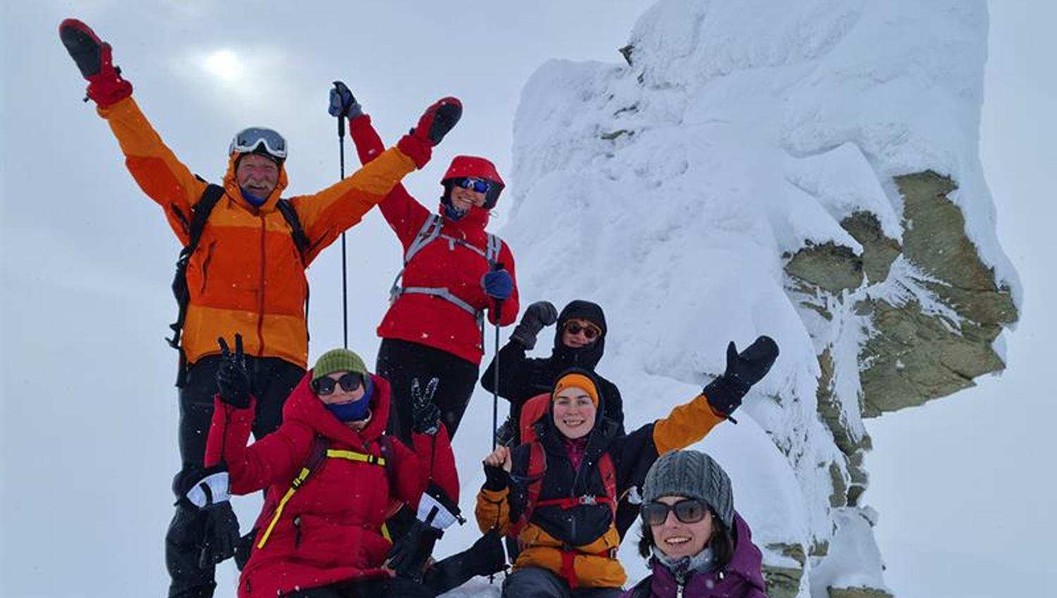 A group of guests cheering for the camera on top of Trollsteinen in snowy conditions